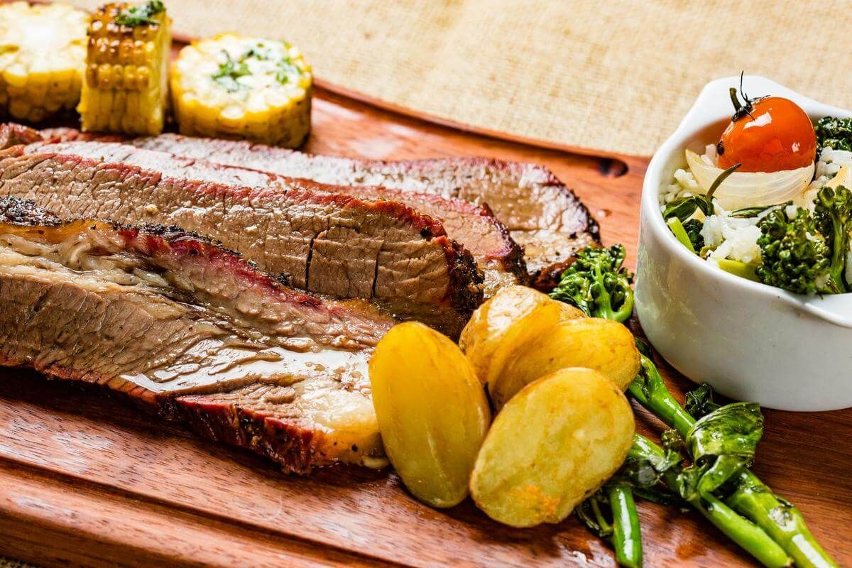 Fotografia de carne assada fatiada com batatas e milho