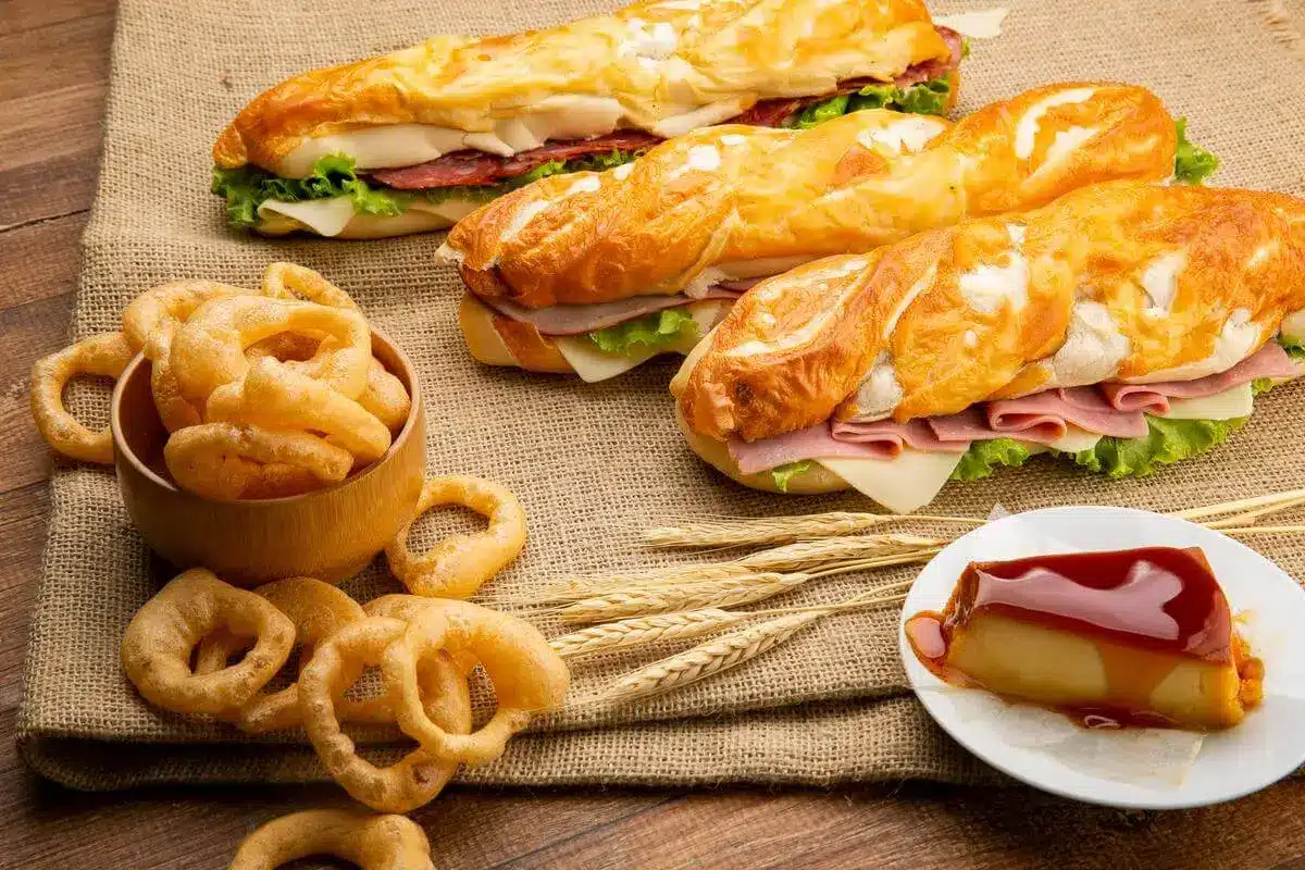 Fotografia de lanches de pão com frios, anéis de cebola e pudim