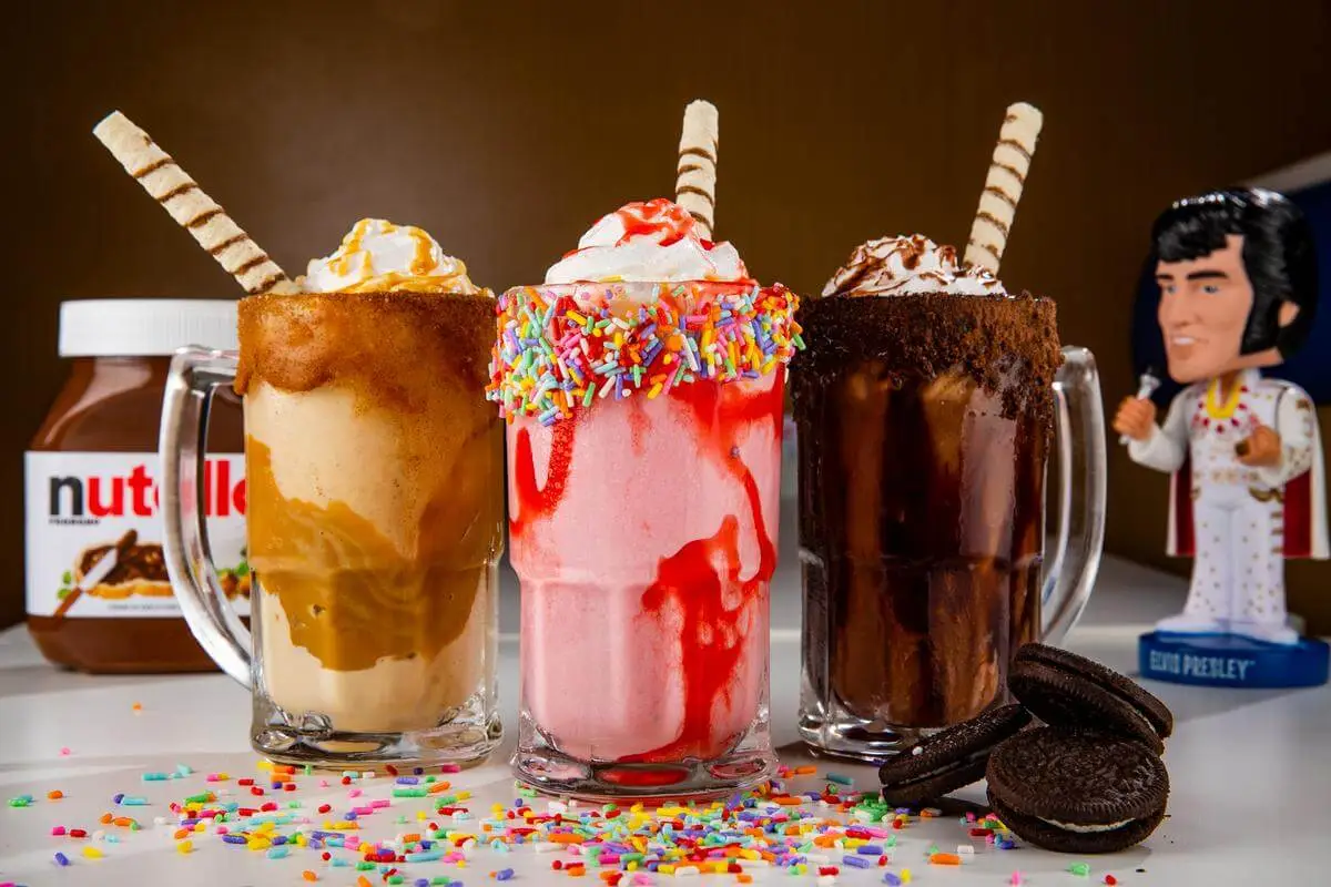 Fotografia de três milkshakes decorados com granulado e biscoitos